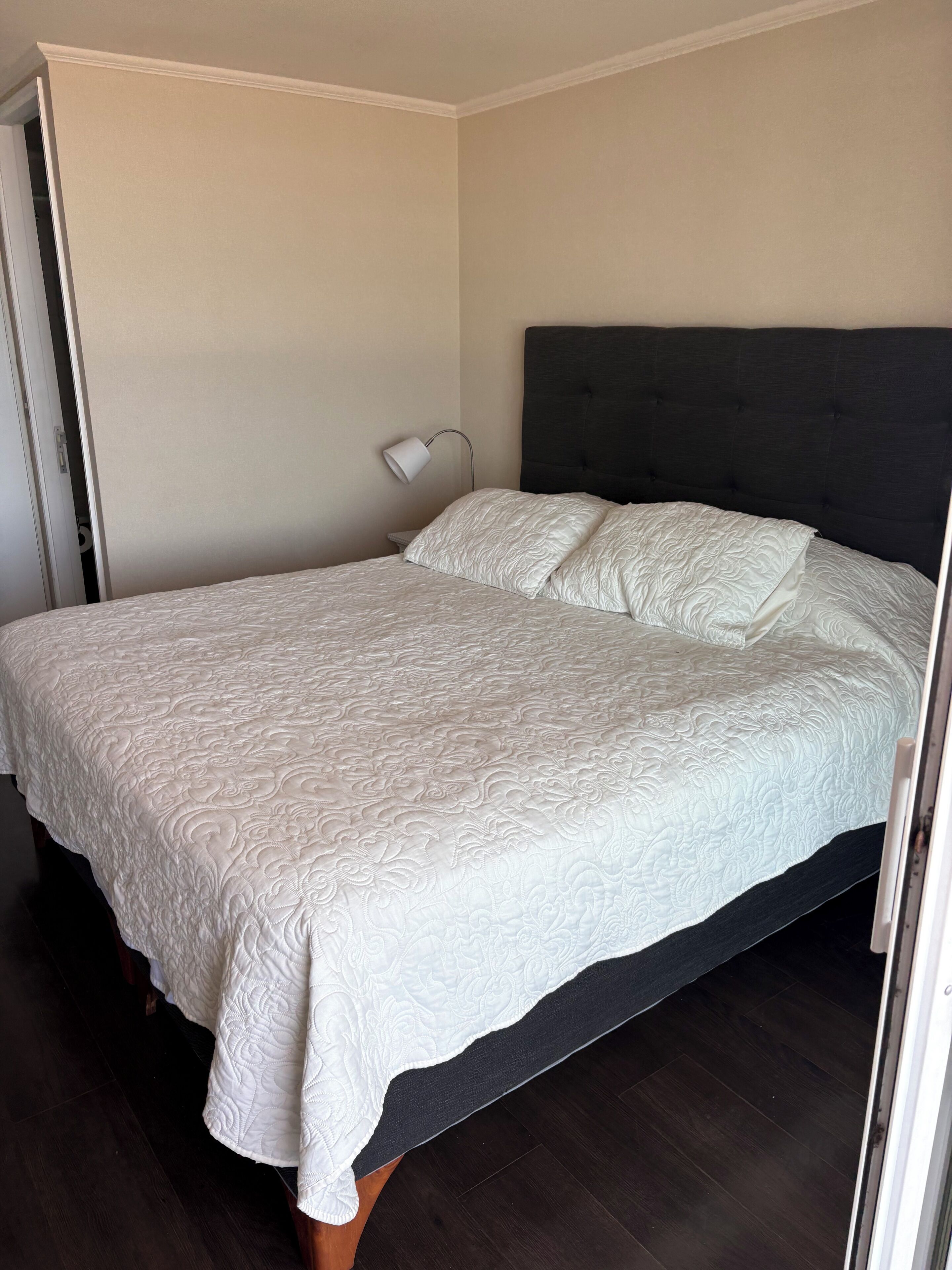 Ein ordentlich bezogenes Bett mit dunkelbrauner Kopfteil und weißer Bettdecke.