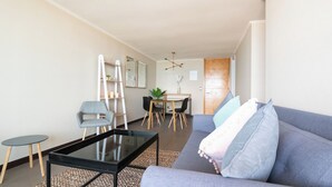 Een moderne woonkamer met een bank, salontafel en stoelen. Er is een eethoek met een tafel en stoelen. Een ladder en planken zijn zichtbaar tegen de muur.