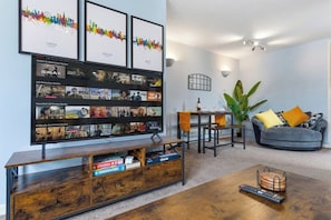 Ein Wohnzimmer mit Flachbildfernseher, einer Holz-Unterhaltungsecke, einem Couchtisch, einer Couch und einem Essbereich mit einer Pflanze.