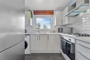 A modern kitchen with white cabinets, a built-in oven, a microwave, and a window with a view of the sky. - 1BR • Free Parking • Home Away From Home • LGW (Crawley)