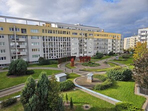 Ein mehrgeschossiges Wohngebäude mit Balkonen, ein angelegter Garten mit einem Rundgangweg und ein kleines Nebengebäude.
