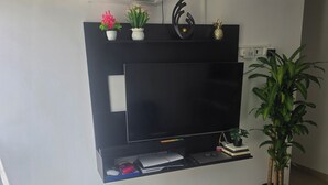Ett vardagsrum med en platt-TV som är monterad på väggen, ett svart soffbord, en krukväxt och en svart matta.