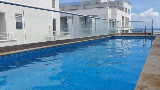 En pool på taket med fri utsikt över havet, ett glasräcke och en modern byggnad i bakgrunden.