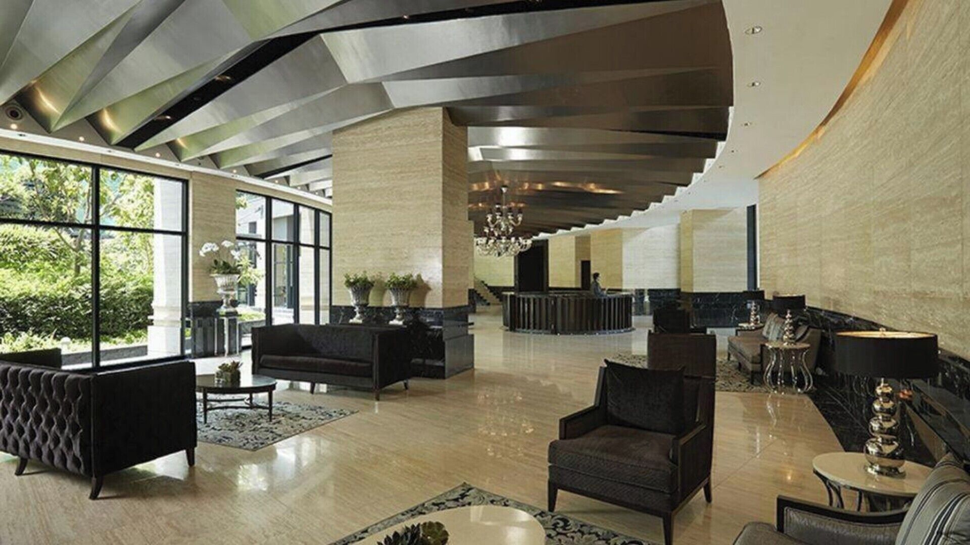 A spacious lobby with a modern design, featuring a reception desk, seating areas, and large windows offering views of greenery.