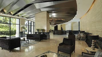 A spacious lobby with a modern design, featuring a reception desk, seating areas, and large windows offering views of greenery.