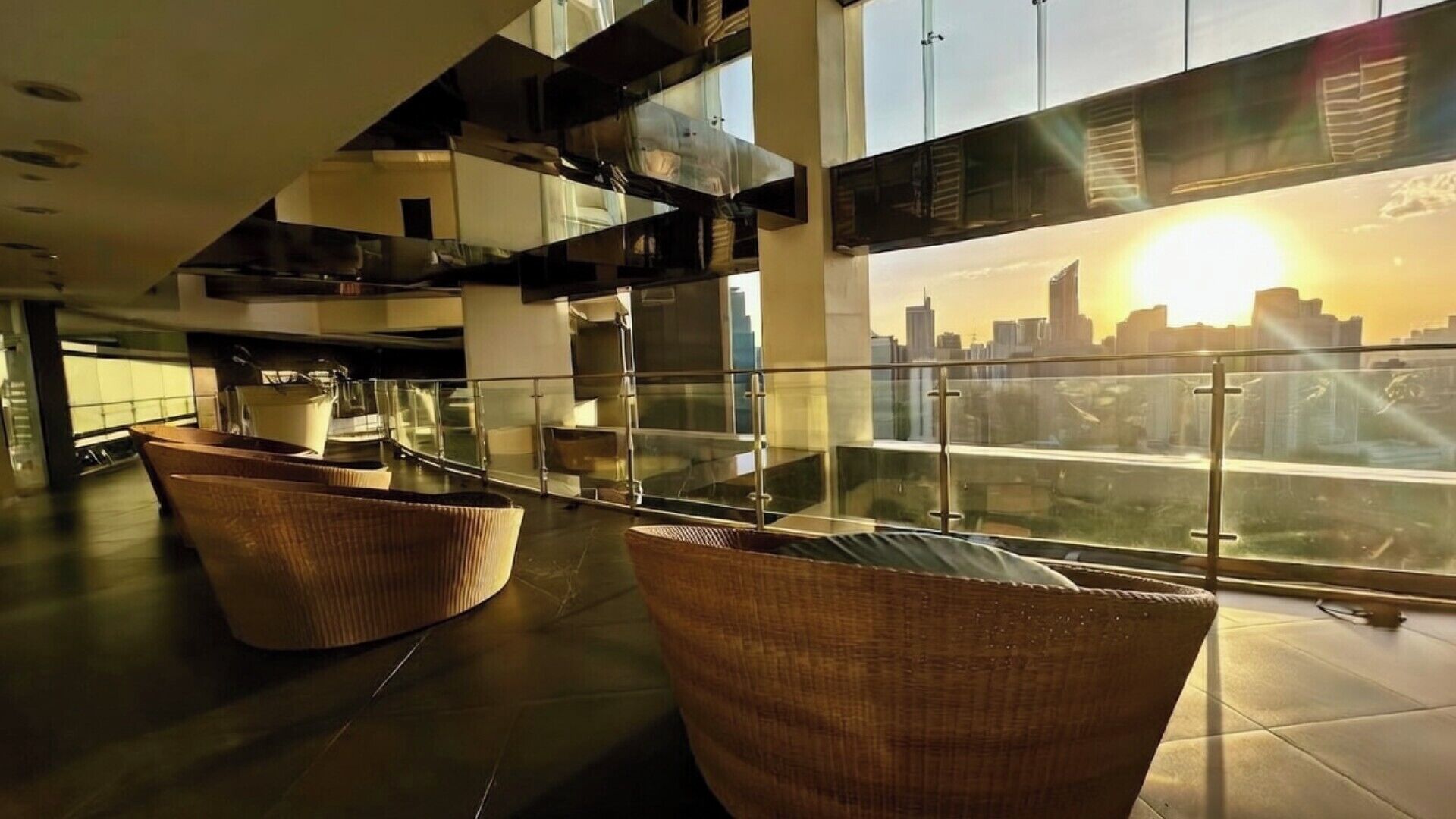 A modern interior with a glass railing, wicker furniture, and a city skyline view.