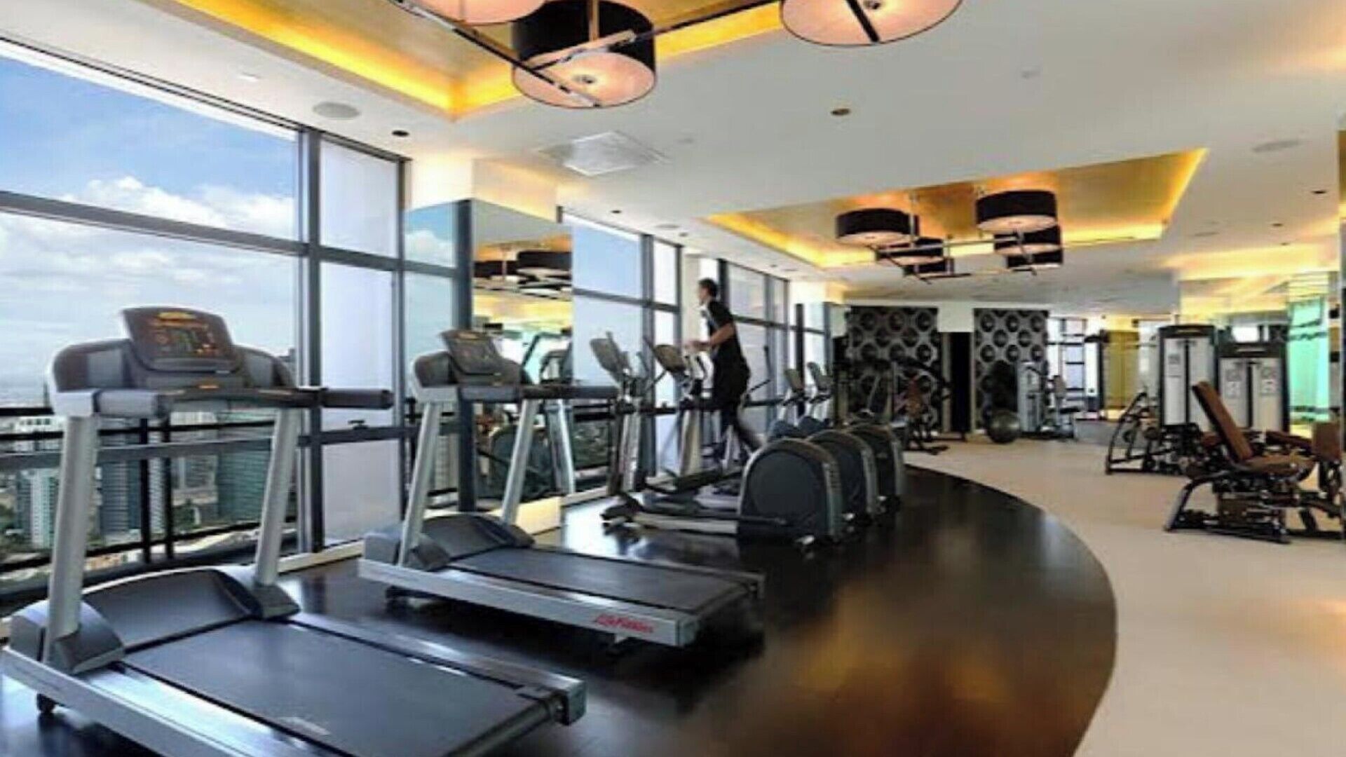 A gym with treadmills, weight machines, and a large window overlooking a cityscape.
