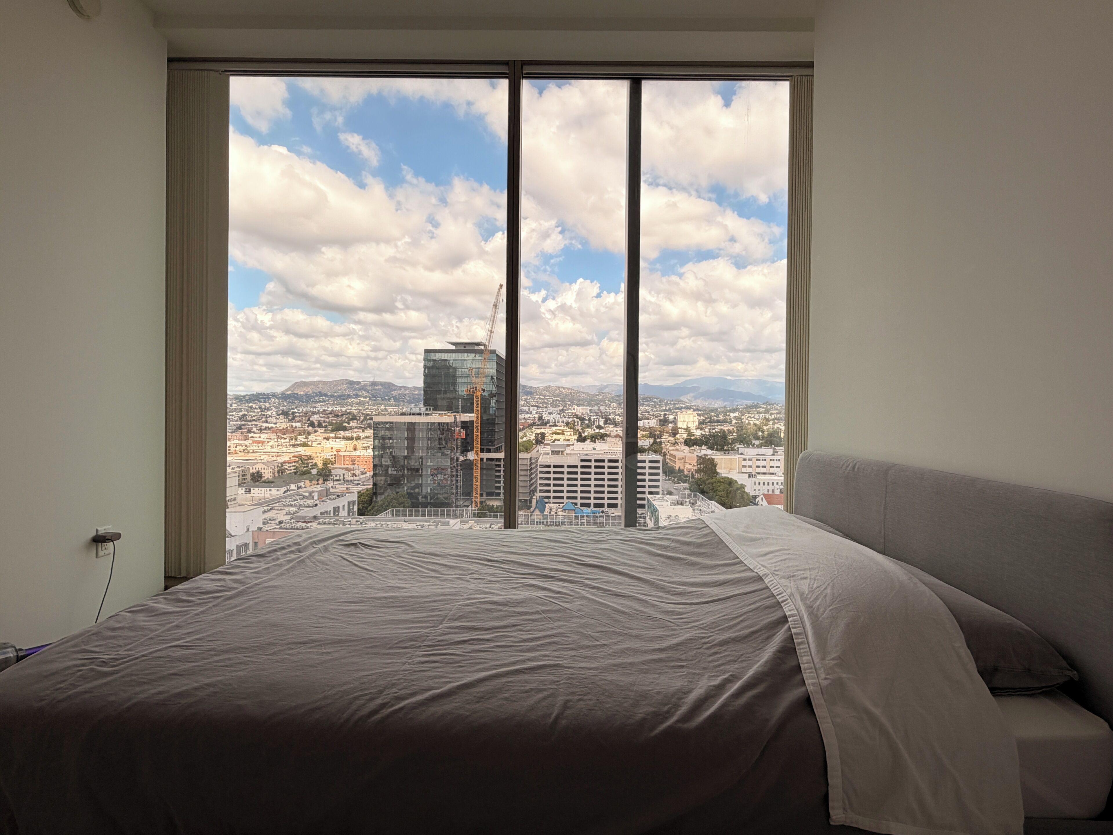 Une chambre avec une grande fenêtre, un lit et une vue sur le paysage urbain.