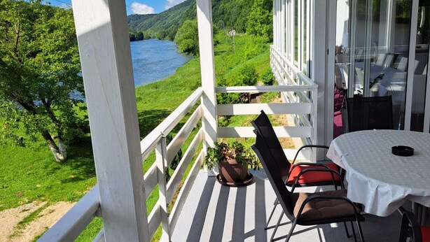 A balcony with a table and chairs, overlooking a river and greenery. - Rooms Denadija Double 1 (Hrvatska Kostajnica)