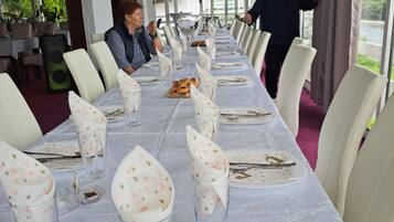 Een lange eettafel met witte tafelkleden en bloemenlinnen, gedekt voor een maaltijd.