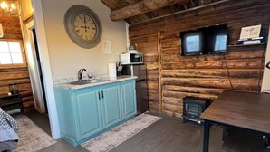 A rustic cabin interior with a kitchen area featuring a blue cabinet, a microwave, and a clock on the wall. - Cozy Rustic Cabin in the City (Richfield)