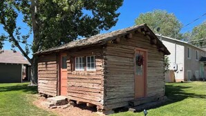 A small, rustic log cabin with a front door, windows, and a porch. - Cozy Rustic Cabin in the City (Richfield)