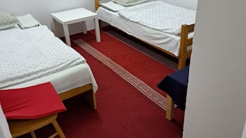 Ett rum med två enkelsängar, ett litet vitt bord, en röd matta och en träbänk.