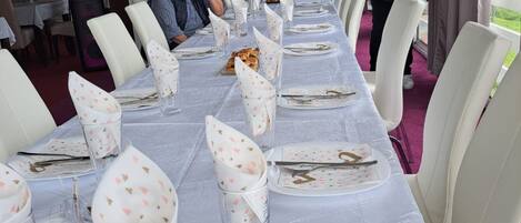 A long dining table set with white chairs, glassware, and plates with a floral pattern.