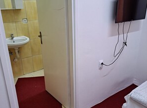 Ein Badezimmer mit Waschbecken, einer Tür und einem an der Wand befestigten Fernseher.