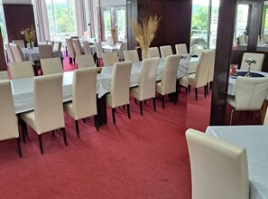 Ein Essbereich mit Tischen, Stühlen, großen Fenstern und einem roten Teppich.