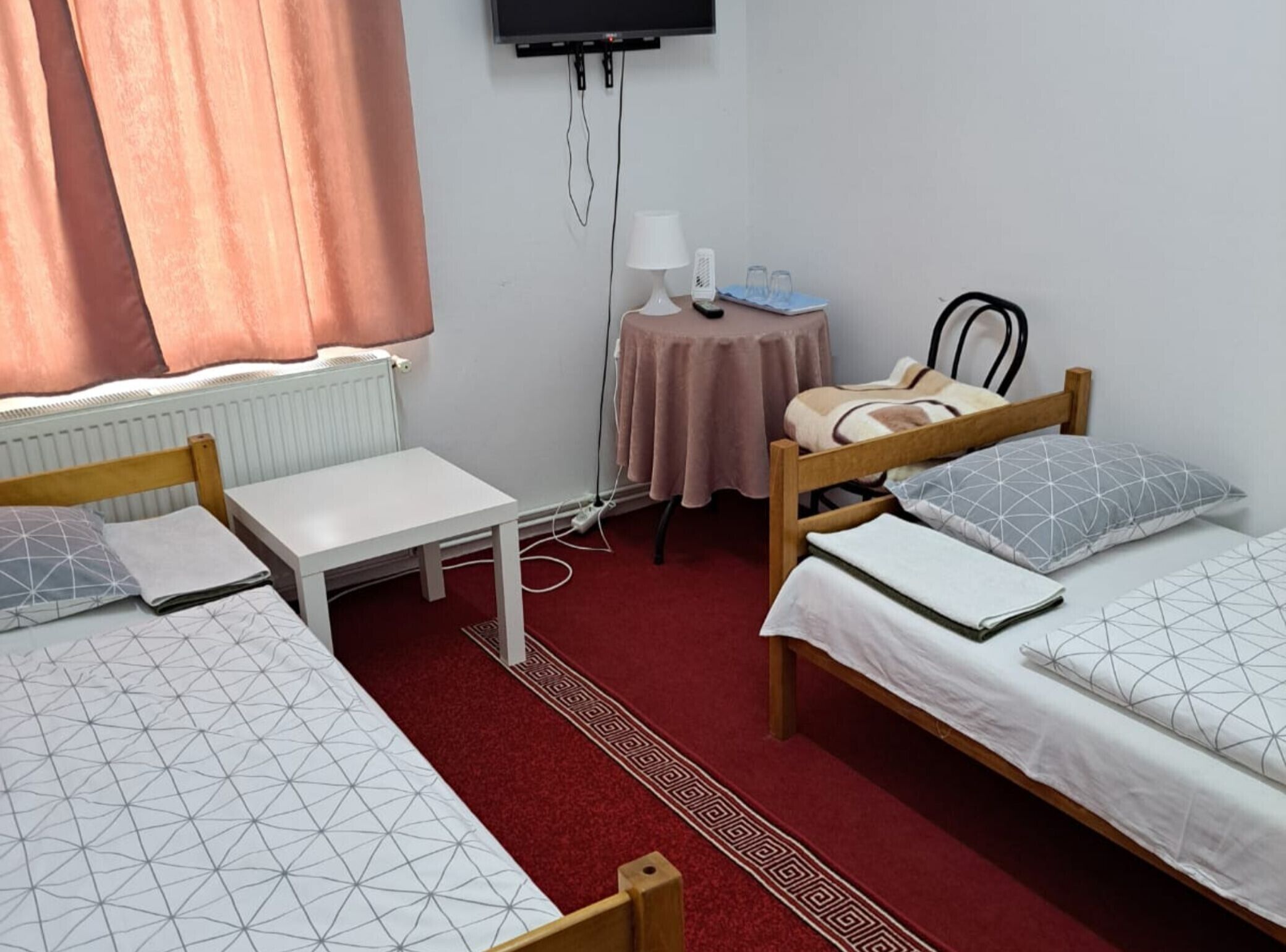 Ein Zimmer mit zwei Betten, einem kleinen Tisch, einer Lampe, einem Fernseher und einer Heizung.