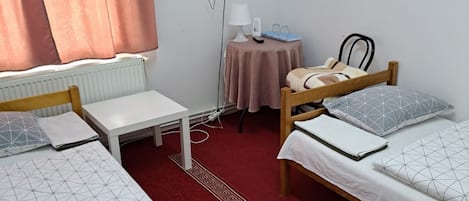 Ein Zimmer mit zwei Betten, einem kleinen Tisch, einer Lampe, einem Fernseher und einer Heizung.