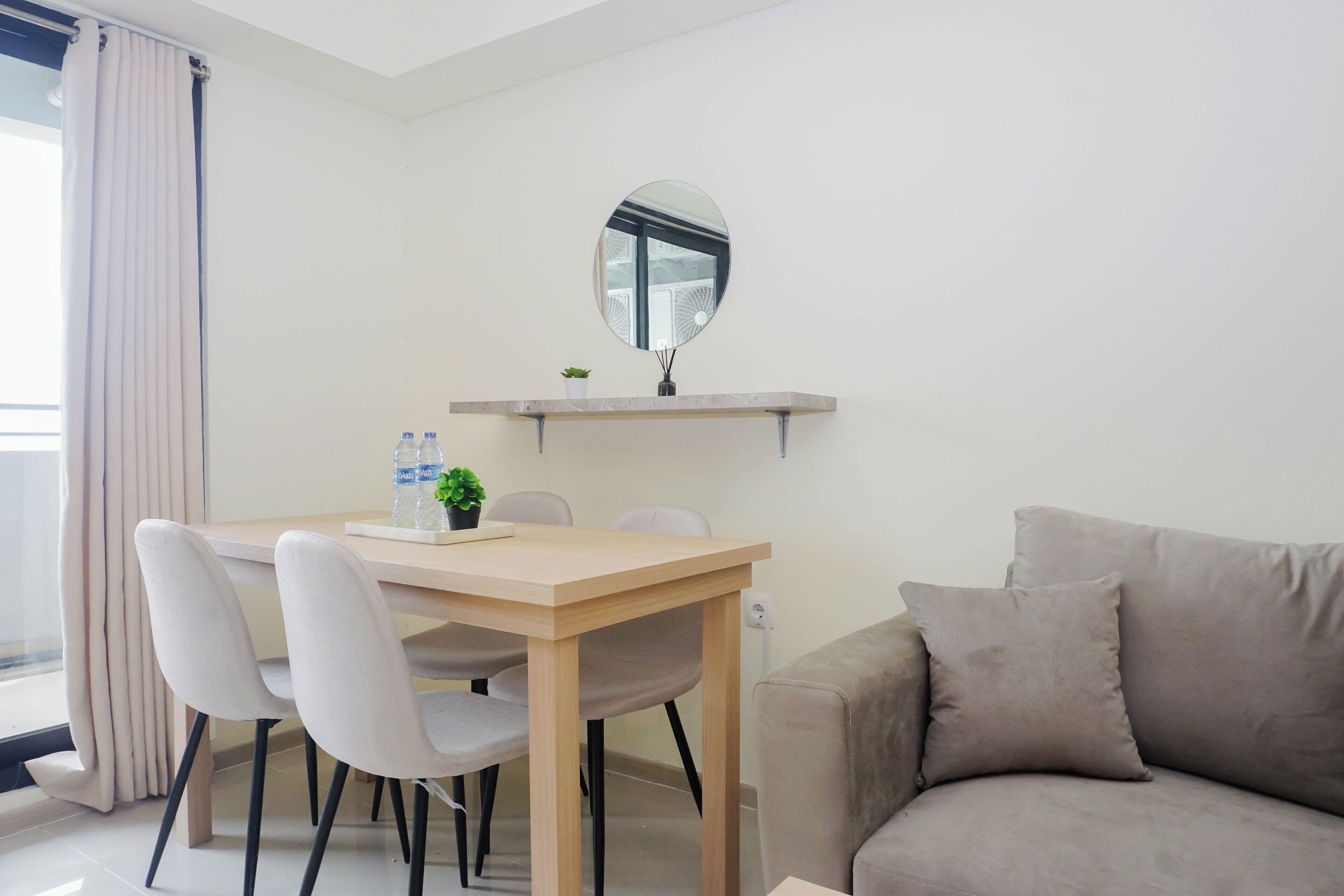Un salon moderne avec une table à manger en bois, deux chaises, un canapé, un miroir rond et une petite plante en pot.