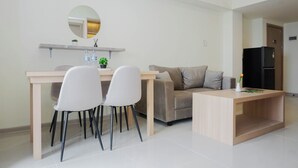 A modern living room with a dining area, a sofa, a coffee table, and a refrigerator. - Neat 3Br For 4 Pax At Meikarta District 2 Apartment (Cikarang)