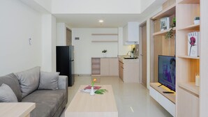 A modern living room with a sofa, coffee table, TV, and kitchen area. - Neat 3Br For 4 Pax At Meikarta District 2 Apartment (Cikarang)