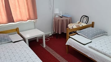 A room with two beds, a small table, a lamp, a TV, and a radiator.