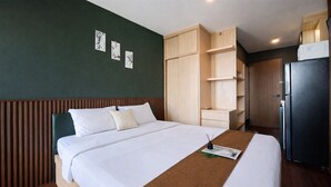 Ein Hotelzimmer mit Bett, Holz-Kopfteil, Kleiderschrank, Kühlschrank und Wandbildern.