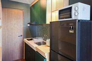 A compact kitchen with a black refrigerator, a microwave, and a sink. - Green Urban Style Studio Room At Apartment Sudimara Forestwalk (South Tangerang)