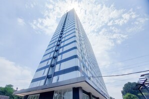 A tall, modern building with a glass facade and a prominent vertical design element. - Green Urban Style Studio Room At Apartment Sudimara Forestwalk (South Tangerang)