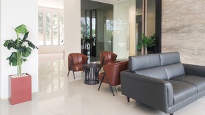 Eine moderne Lobby mit grauem Sofa, braunen Ledersesseln, einem kleinen runden Tisch und einem Blumentopf.