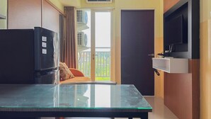 Une cuisine compacte avec une table en verre, un réfrigérateur, un téléviseur fixé au mur et un balcon avec vue.