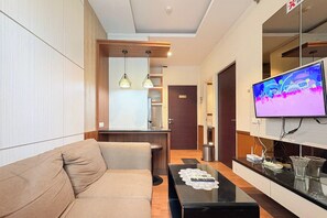 A modern living room with a sofa, a flat-screen TV, a coffee table, pendant lights, and a view of the hallway. - Cozy Stay 2Br Apartment At Malioboro City (Depok)