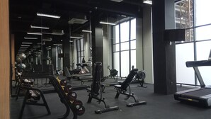 A gym with various exercise equipment, large windows, and a mirrored wall. - Minimalist Studio Loft Apartment At Kingland Avenue (South Tangerang)