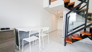 A modern kitchen with a white countertop, two white chairs, a wooden cabinet, and a glass staircase. - Affordable Price Studio Loft At Kingland Avenue Apartment (South Tangerang)