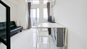 A modern, well-lit room with a white table, two chairs, a black sofa, and a large window with curtains. - Affordable Price Studio Loft At Kingland Avenue Apartment (South Tangerang)