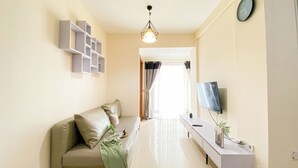 A living room with a sofa, a TV, a desk, and a hanging light fixture. - Cozy Living 2Br Apartment At Green Bay Condominium (Jakarta)