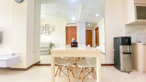 A modern kitchen with a refrigerator, a water dispenser, and a dining area with a table and chairs. - Cozy Living 2Br Apartment At Green Bay Condominium (Jakarta)