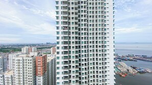 A high-rise building with multiple balconies, a marina with boats, and a distant cityscape. - Cozy Living 2Br Apartment At Green Bay Condominium (Jakarta)