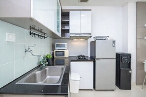 A modern kitchen with stainless steel appliances, a sink, a small refrigerator, and a water dispenser. - Spacious And Contemporary 2Br Apartment Green Bay Condominium (Jakarta)