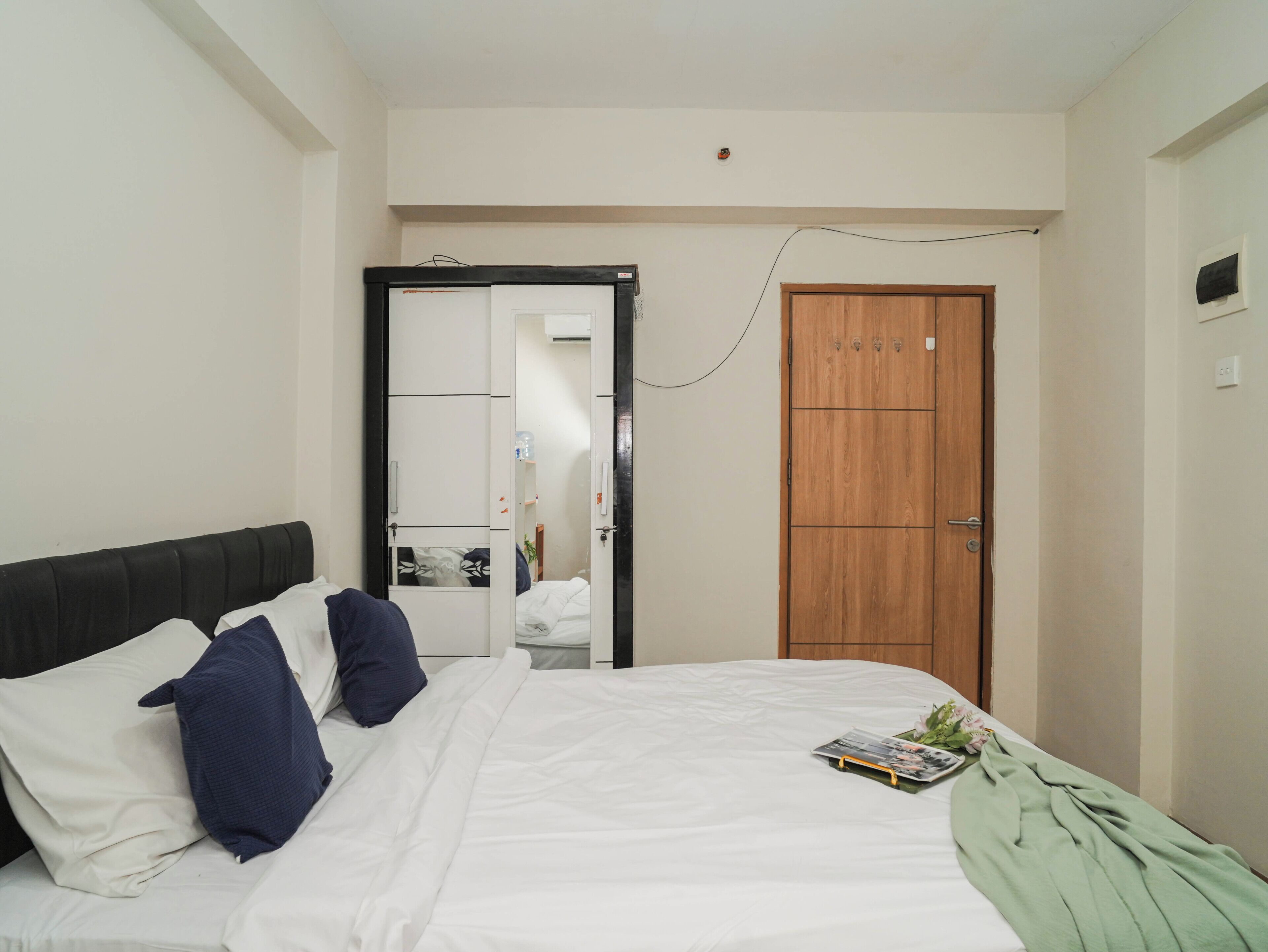 Een slaapkamer met een bed, kussens, een groene deken, een houten garderobe en een deur.