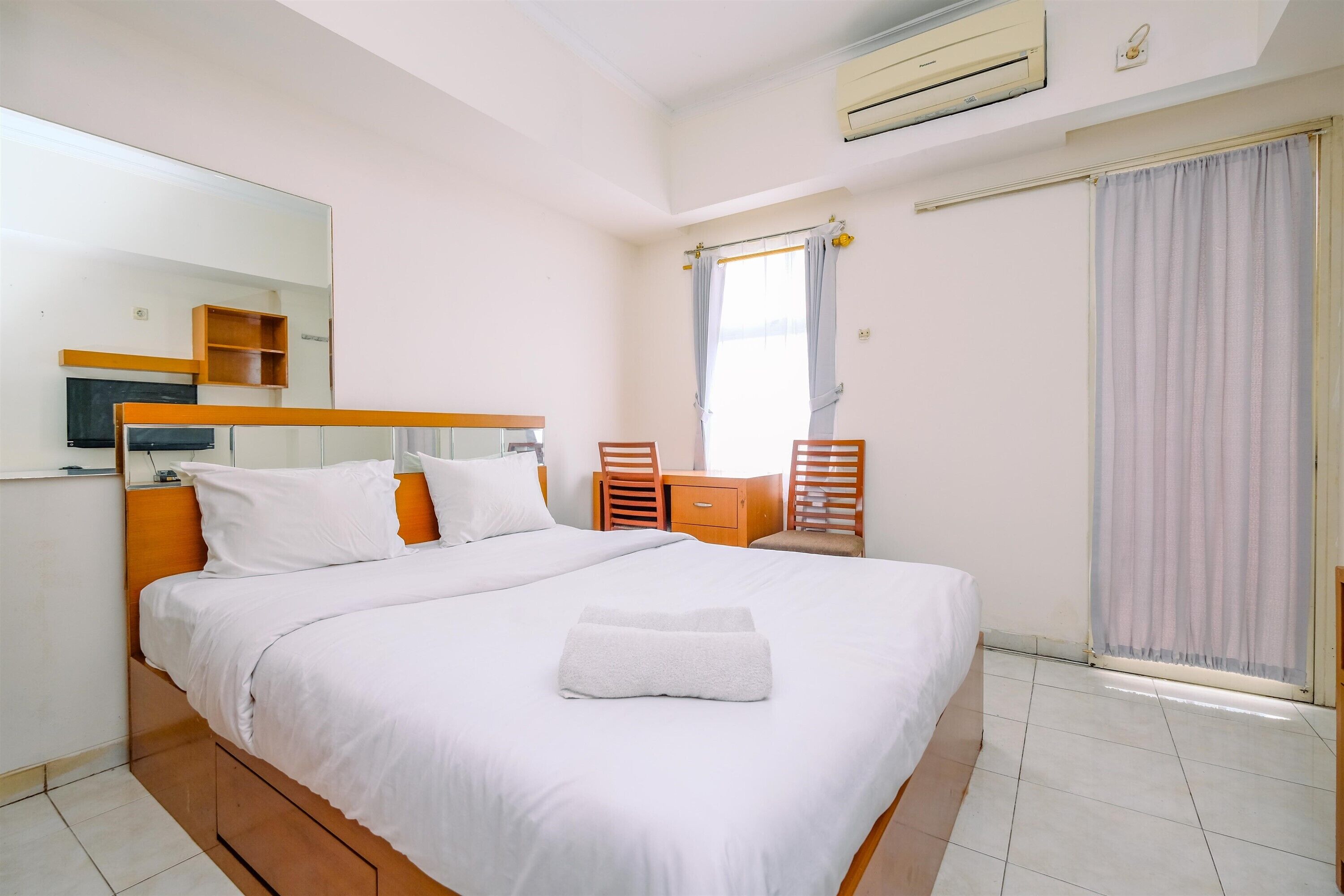 A hotel room with a bed, a desk, a chair, a mirror, and a window with curtains.