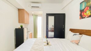 A hotel room with a bed, a small kitchenette, a mirror, and a painting on the wall. - Convenient Studio Near Universitas Indonesia At Margonda Residence 2 (Bogor)