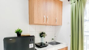 A compact kitchen with wooden cabinets, a black refrigerator, a small sink, and a potted plant. - Convenient Studio Near Universitas Indonesia At Margonda Residence 2 (Bogor)