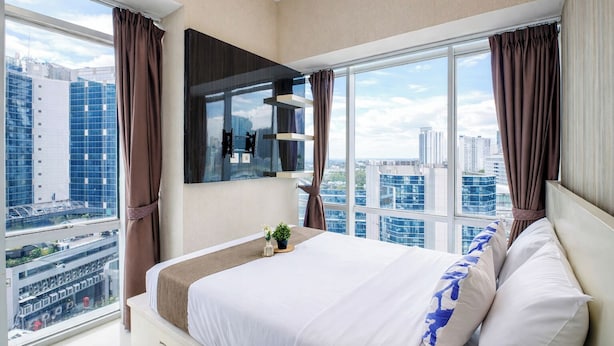 Una habitación de hotel moderna con una cama grande, un televisor montado en la pared y vistas a la ciudad.
