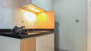 A compact kitchen with a gas stove, a sink, and a modern light fixture. - Comfy Modern Look Studio Room At Apartment Grand Dharmahusada Lagoon (Surabaya)