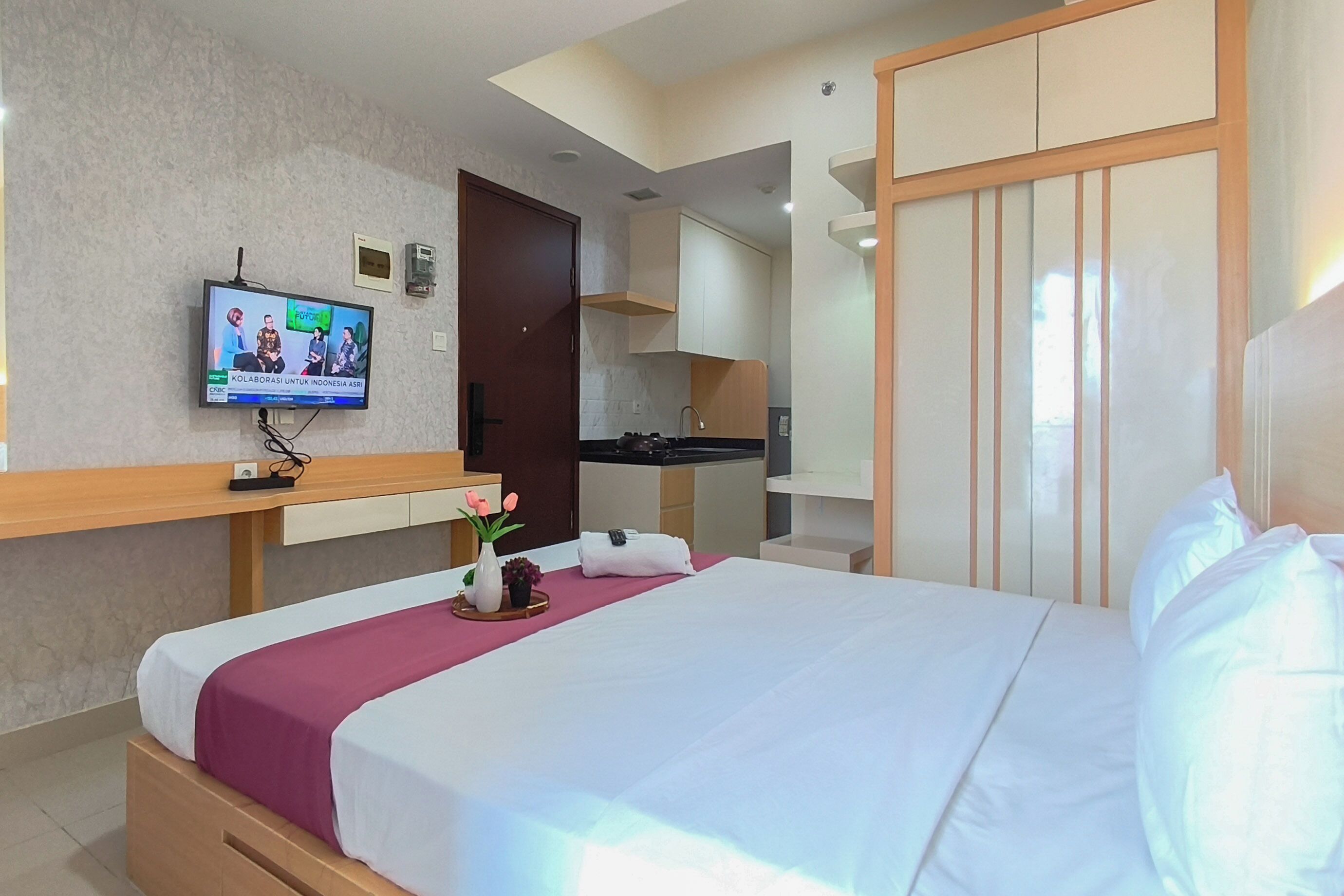 Una habitación de hotel con cama, televisión, kitchenette y armario.