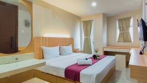 A hotel room with a bed, bedside table, desk, and a large mirror. - Comfy Modern Look Studio Room At Apartment Grand Dharmahusada Lagoon (Surabaya)