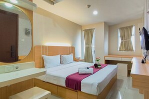 A hotel room with a bed, bedside table, desk, and a large mirror. - Comfy Modern Look Studio Room At Apartment Grand Dharmahusada Lagoon (Surabaya)
