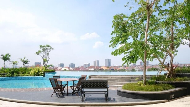 A rooftop pool area with a table and chairs, surrounded by greenery and overlooking a cityscape. - Comfy Modern Look Studio Room At Apartment Grand Dharmahusada Lagoon (Surabaya)