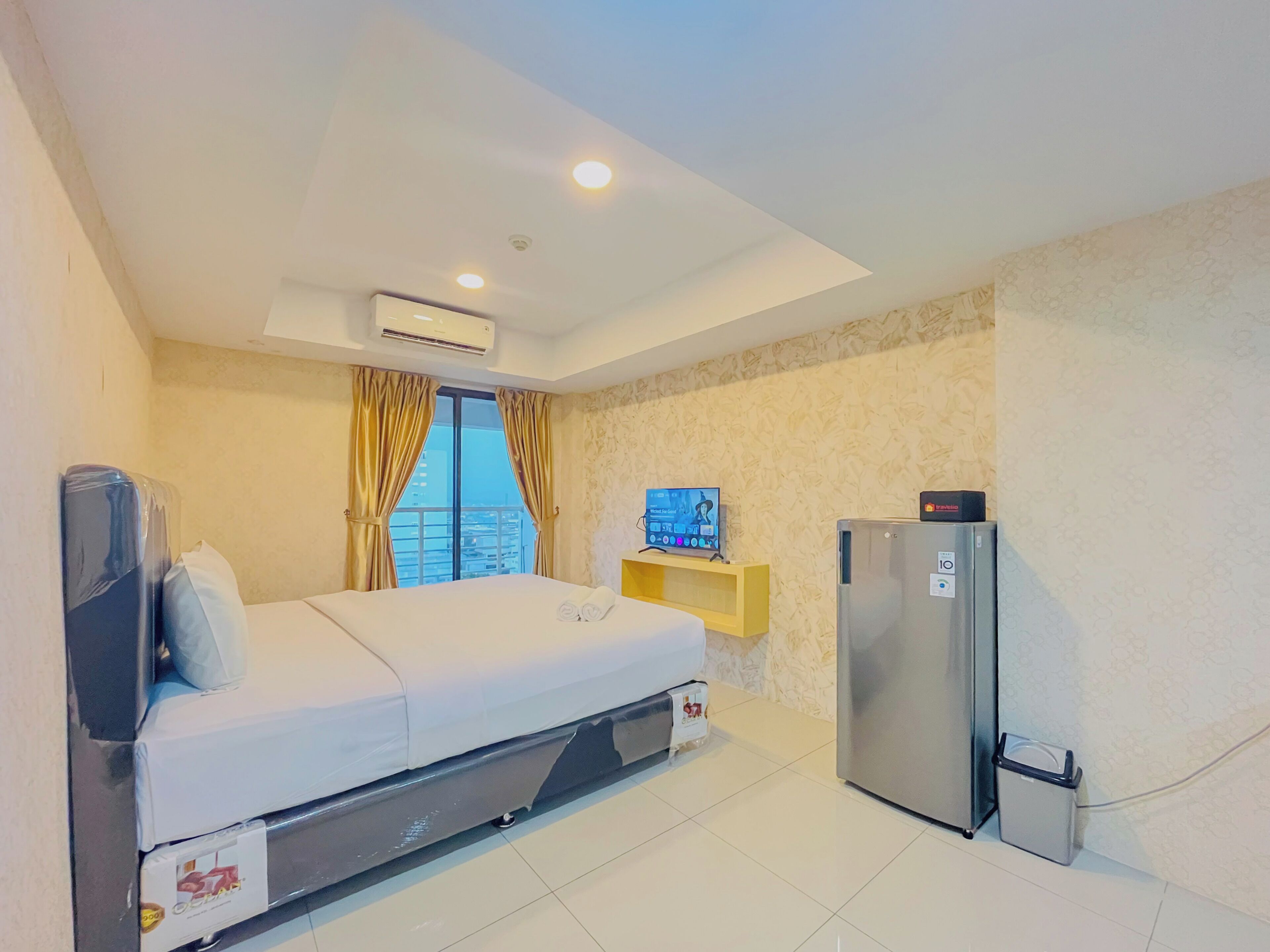 A hotel room with a bed, a TV, a refrigerator, and a window with curtains.